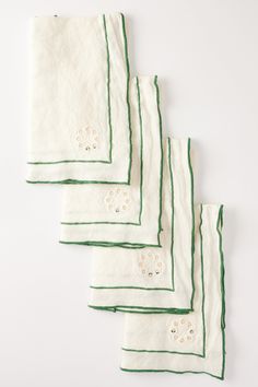 four white and green napkins with embroidered flowers on them, lined up against a white background