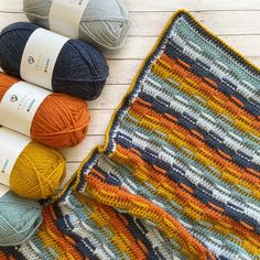 three balls of yarn sitting next to each other on a wooden surface with two crocheted afghans