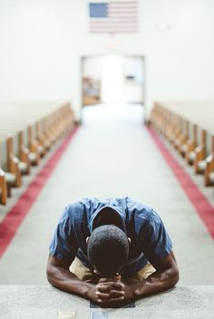 a man sitting on the ground in front of rows of pews with his head down