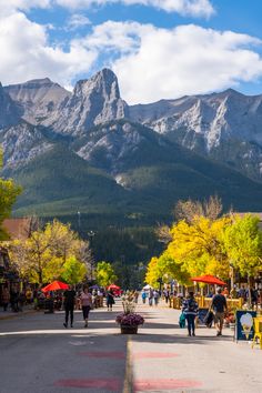 people are walking down the street in front of some mountains and tables with umbrellas