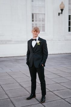 a young man in a tuxedo poses for a photo outside the state capitol building