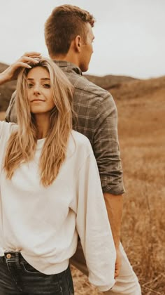 a man standing next to a woman on top of a dry grass covered field,