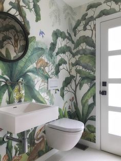 a bathroom with tropical wallpaper and a white toilet