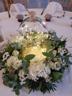 flowers and greenery are arranged around a glass dome on a table with white linens