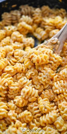 macaroni and cheese being stirred with a wooden spoon