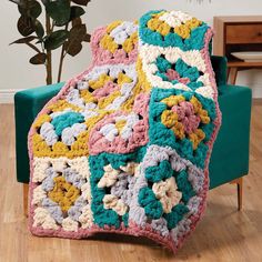 a crocheted blanket sitting on top of a green chair next to a potted plant