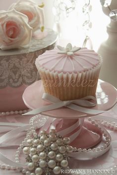 two cupcakes are sitting on pink plates with pearls and flowers in the background