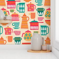 colorful teapots and cups are on the shelf in front of a wallpaper