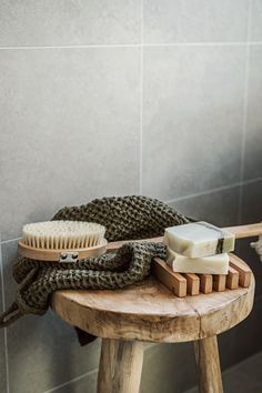 a wooden stool with a brush, soap and other items on it next to a tiled wall