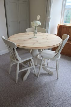 a round wooden table with four chairs around it in a living room next to a window