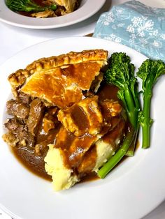 a plate with meat, gravy and broccoli on it next to another plate