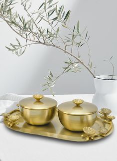 two gold covered dishes sitting on top of a table next to a vase with an olive branch in it