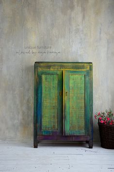 an old green cabinet sitting next to a potted plant in front of a wall