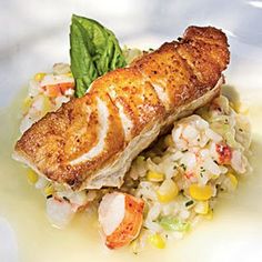 a piece of fish and rice dish on a white plate with green leafy garnish