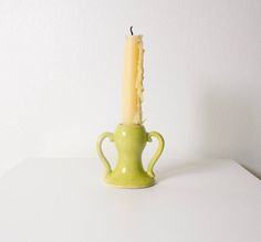 a small green vase with a lit candle in it on a table next to a white wall