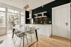 a dining room table and chairs in front of an open kitchen with lots of windows