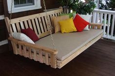 a wooden porch swing with pillows on the front and back sides hanging from it's chains