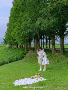 two women dressed in white standing next to each other near trees and grass on the ground