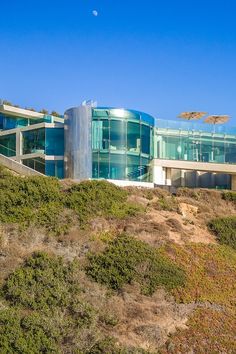 a large glass building sitting on top of a hill next to a hillside covered in grass