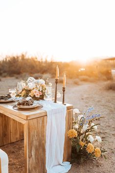 a table set up with flowers and candles for an outdoor dinner party in the desert