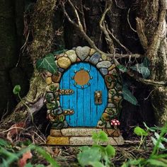 a small blue door sitting in the middle of a forest next to a large tree