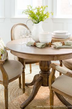 a dining room table and chairs with plates, glasses and flowers on the centerpiece