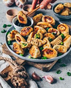 someone dipping sauce on some dumplings in small bowls next to garlic and green onions