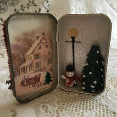 an open tin box with a small christmas tree and snowman in front of it