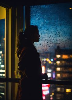 a woman standing in front of a window with raindrops on the windowsill