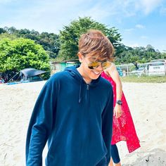 a young boy walking on top of a sandy beach next to a woman in a red dress