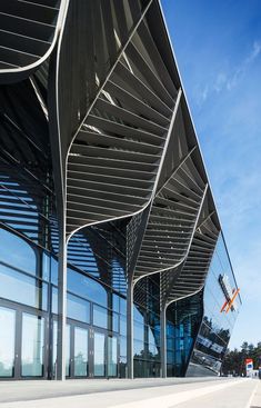 an architectural building with curved metal roofing and glass windows on the outside, against a blue sky