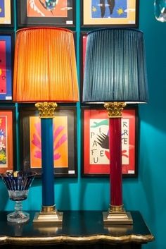 two lamps sitting on top of a table next to a blue wall with framed pictures