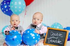 two babies are sitting next to each other in front of balloons and a sign that says double trouble