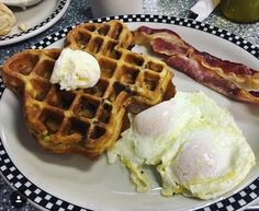 a white plate topped with waffles and eggs next to bacon on a table