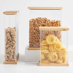 three glass containers filled with different types of pasta and pretzels in front of each other