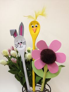 three plastic spoons in a vase with flowers and bunny ears on them, one is yellow