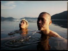 two people swimming in the water with mountains in the background