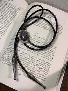 an open book with a black leather cord on top of it and two silver beads hanging from the end