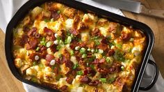 a casserole dish with bacon, cheese and green onions in it on a table