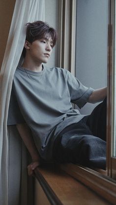 a young man sitting on top of a window sill next to a white curtain