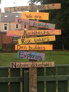 a wooden sign with words written on it in front of a green fence and some houses