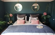 a bed with two mirrors above it and flowers on the nightstands next to it