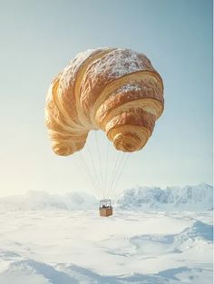 a croissant is being lifted by a parachute in the air over snow covered mountains