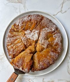 a white plate topped with a cake covered in powdered sugar next to a wooden spatula