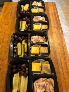 four trays filled with different types of food on top of a wooden countertop