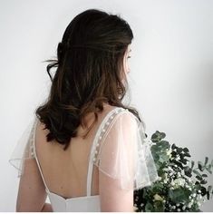 the back of a woman in a wedding dress holding a bouquet of flowers and greenery