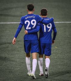 two soccer players in blue uniforms are standing on the field and hugging each other's shoulders