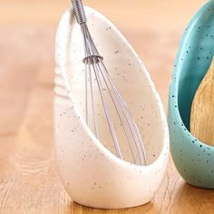 two ceramic bowls with whisk attachments sitting on a wooden table next to each other