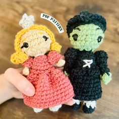 two crocheted dolls are being held by someone's hand