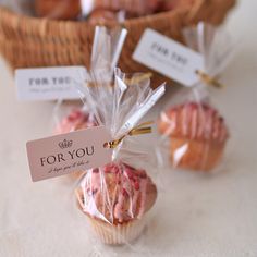 small cupcakes wrapped in cellophane are sitting on a table next to a basket